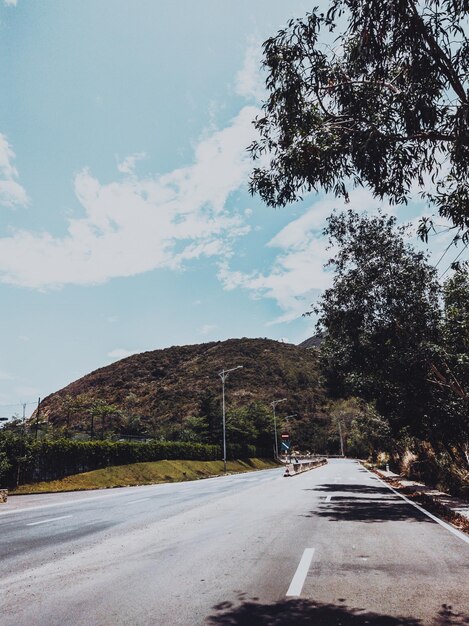 Trockener Asphalt, leere Autostraße mit Betonbarriere und Markierungslinien an einem sonnigen Sommertag mit blauem, bewölktem Himmel Hintergrund des Autoreisekonzepts Geschichten Hochformat Dunkelgrüner Stil