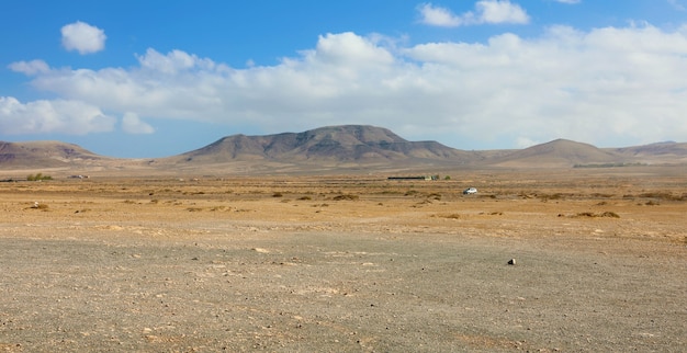 Trockener Boden unter weißen Wolken und blauem Himmel mit Bergen auf der Insel Fuerteventura