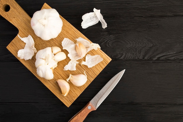 Trockener Knoblauch auf dem braunen Schneidebrett auf dem schwarzen Holzhintergrund. Ansicht von oben. Platz kopieren.