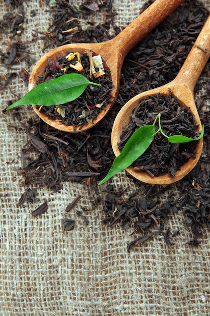 Trockener Tee mit grünen Blättern in Holzlöffeln auf Sackleinenhintergrund
