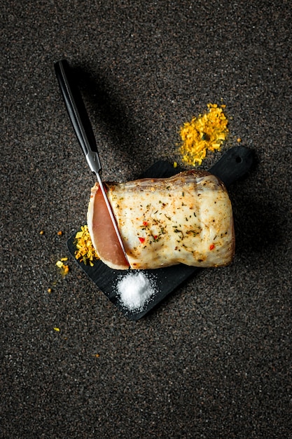Trockengehärtetes Fleisch mit Gewürzen und Salz, Messer schneidet eine Scheibe, auf dunkelgrauer Oberfläche