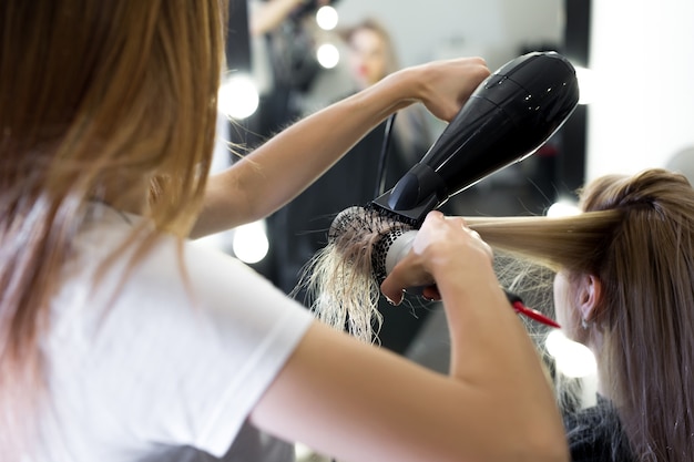 Trocknen Sie lange blonde Haare mit Fön und Rundbürste