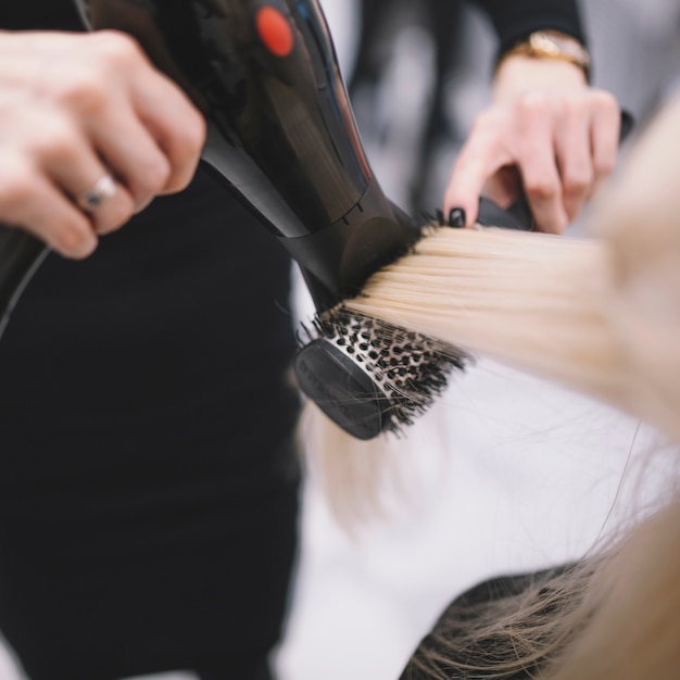 Trocknendes Haar des anonymen Stylisten mit Bürste