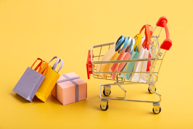Trolley-Wagen mit bunten Papiereinkaufstüten isoliert Kreative Idee für den Online-Shopping-Supermarkt-Rabatt und Sommerverkaufskonzept