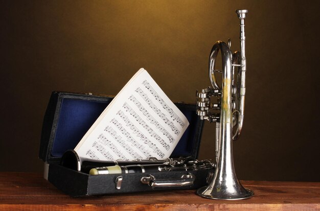 Trompeta antigua y clarinete en caso de mesa de madera sobre fondo marrón