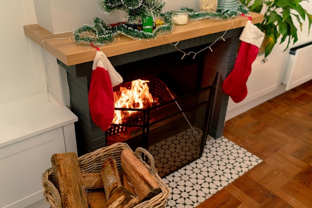 Foto troncos de madera en una canasta junto a la chimenea con un calcetín navideño. navidad, festividad y tradición en casa.