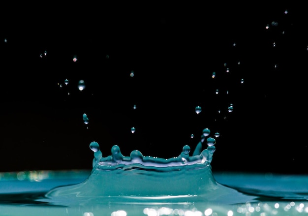 Tropfen, die auf krümmendes Wasser gegen schwarzen Hintergrund fallen