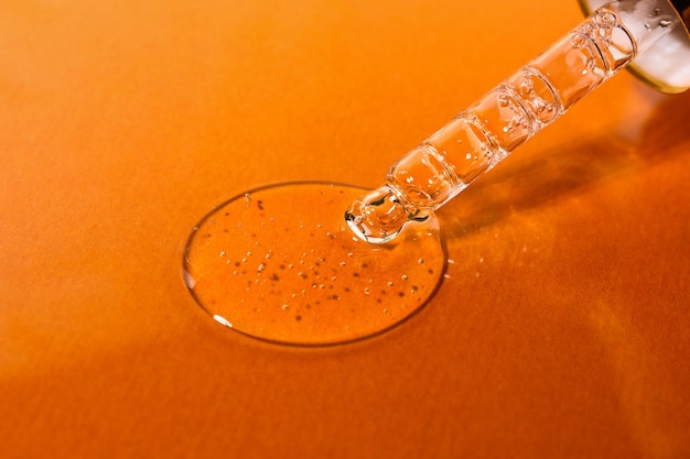 Tropfer mit durchsichtigem kosmetischem flüssigem Serum für Körper- und Gesichtsnähbild auf orangefarbenem Hintergrund