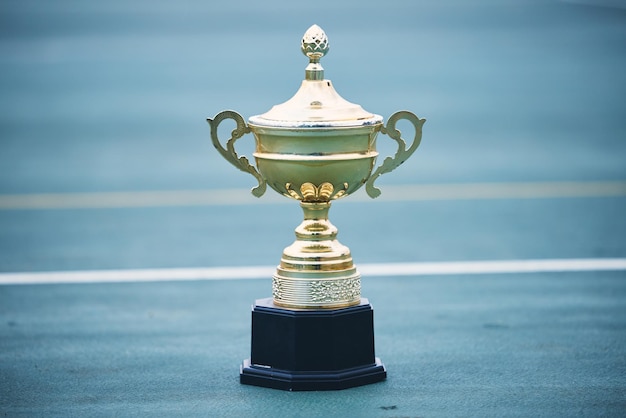 Trophäe und Ziel mit einem Sportpokal auf einem leeren Platz im Freien für den Sieger, Meister oder Sieger. Goldenes Tor und Erfolg mit einem Preis auf dem Boden draußen in einem Stadion oder einer Sportarena