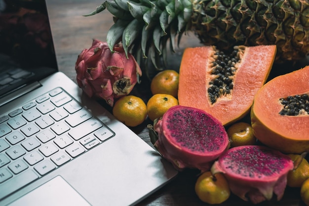 Tropische Früchte in der Nähe eines modernen Laptops auf Holzhintergrund Veganer Lebensstil