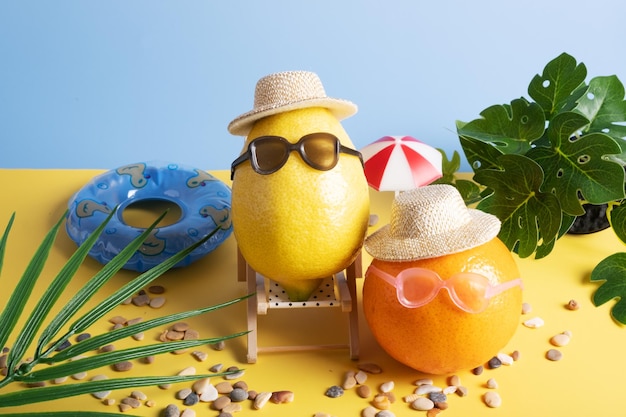 Tropische Früchte Zitrone und Mandarine in Hüten und Sonnenbrillen am Strand