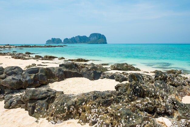 Tropische Meereslandschaft mit Felsen am Sandstrand und felsiger Insel am Horizont