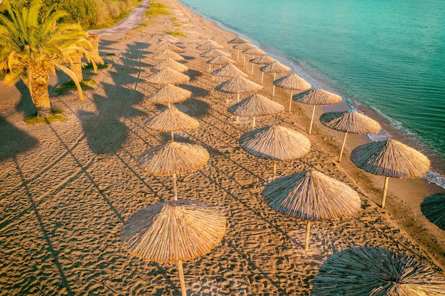 Tropische Strandlandschaft mit Sonnenschirmen und Palmzweigen Strohsonnenschirme am Strand bei Sonnenuntergang Blick auf das Meer von oben