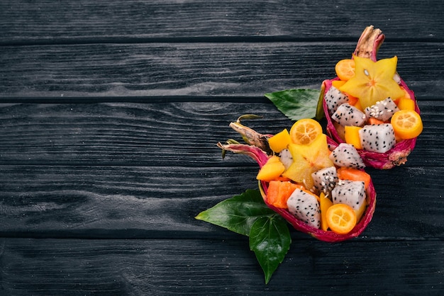 Tropischer Fruchtsalat serviert in einer halben Drachenfrucht Papaya Rambutan Tamarinde Kaktusfrucht Mango Auf einem hölzernen Hintergrund Ansicht von oben