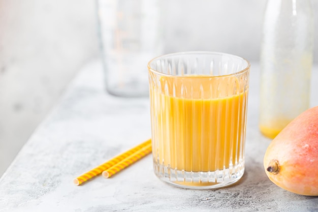 Tropischer Mango-Smoothie in einem Glas und frische Mango auf hellem Hintergrund. Mango-Shake. Konzept der tropischen Früchte.