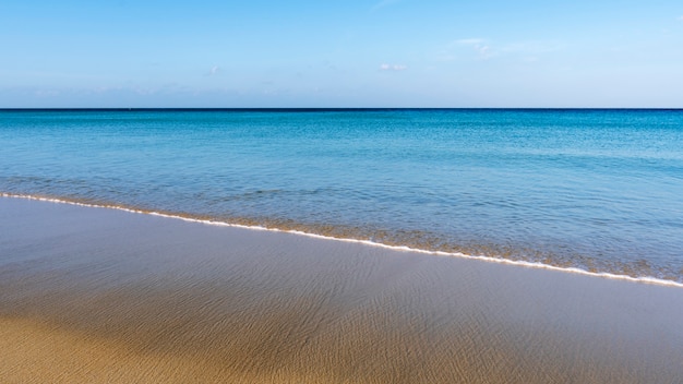 Tropischer sandiger Strand mit blauem Himmel und Welle, die auf sandigem Ufer zusammenstößt