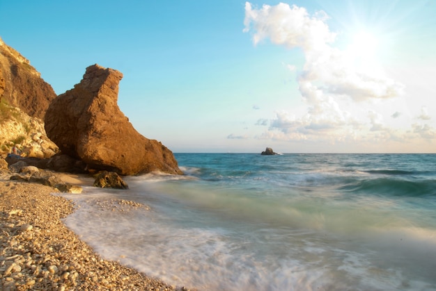 Tropischer Strand auf dem Sonnenuntergang mit Wasser und Felsen.