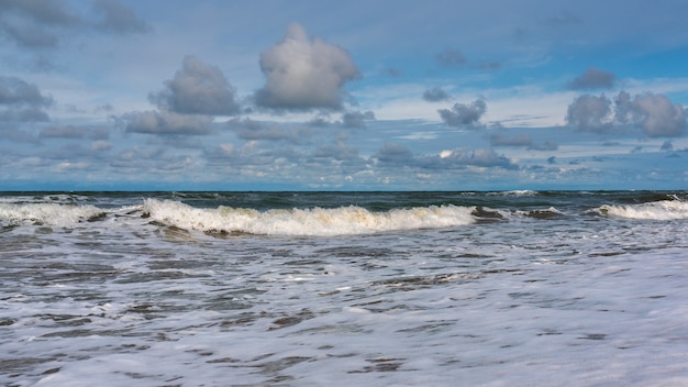 Tropischer Strand, kleine Wellen und blauer Himmel mit Wolken