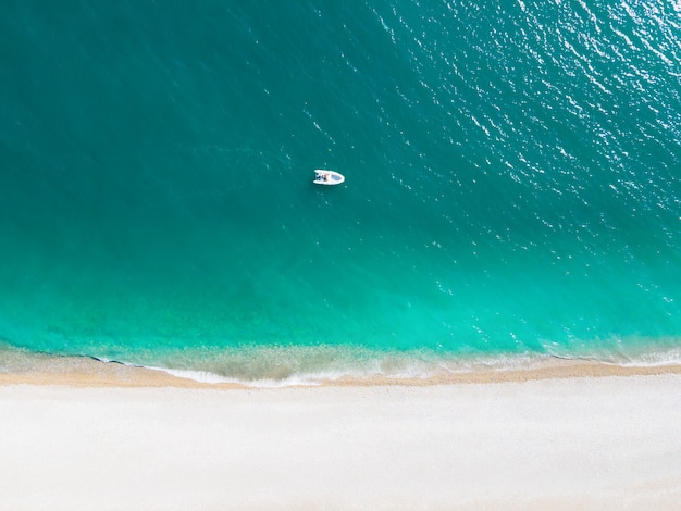 Tropischer Strand mit türkisfarbenem Wasser und weißen Kieselsteinen. Boot nahe der Küste. Drohnenansicht aus der Luft. Sommer Natur Hintergrund. Reisezielkonzept
