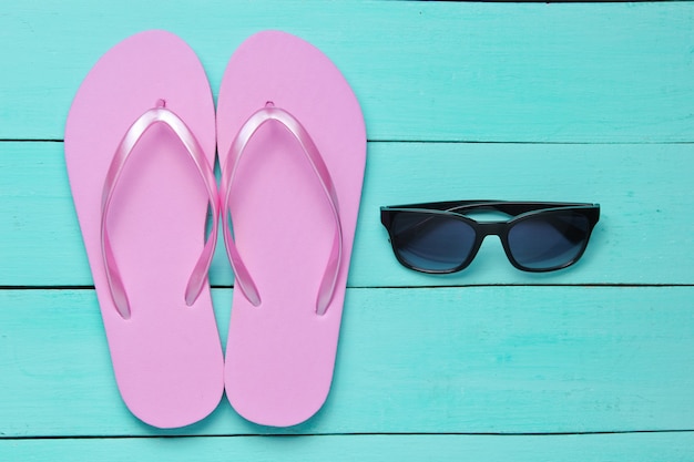 Tropischer Strandlebensstil. Flip Flops und Sonnenbrille auf blauem Holzhintergrund. Sommerhintergrund. Draufsicht