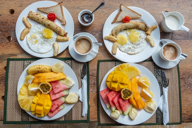 Tropisches Frühstück mit Fruchtkaffee und Rührei und Bananenpfannkuchen für zwei Personen am Strand in der Nähe des Meeres Tischdekoration mit Draufsicht