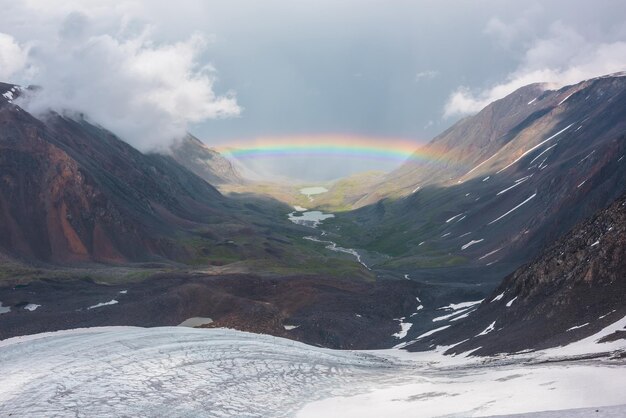 Foto trostlose landschaft mit lebendigem regenbogen über einem bergsee trostlose landschaft mit hellem regenbogen über einem gletscher und einem gletschersee im bergtal top-aussicht auf farbenfrohen regenbogen und niedrige wolken in den bergen