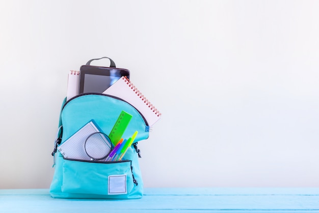 Trouxa completa da escola de turquesa com artigos de papelaria na tabela.