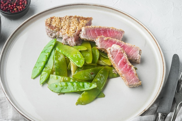 Trozo de atún asado en ajonjolí con cebolletas y guisantes, en plato, sobre piedra blanca