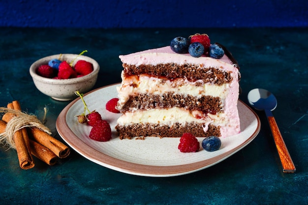 Un trozo de bizcocho de chocolate con relleno de queso crema sobre fondo azul oscuro de cerca Bayas sobre decoración de crema rosa Foto de alta calidad