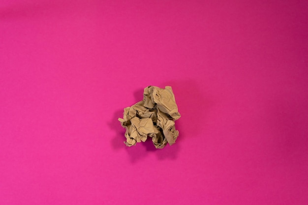 Un trozo de bola de papel marrón arrugado sobre un fondo rosa