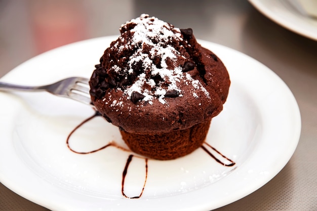 Un trozo de brownie de chocolate con salsa de chocolate y azúcar en polvo sobre una placa blanca en un café concepto de comida chatarra