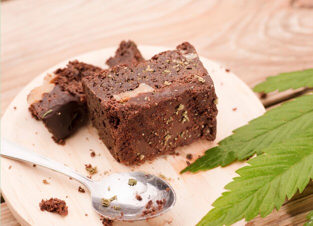 trozo de brownie con marihuana en tablero de madera con cuchara y hoja de cannabis verde