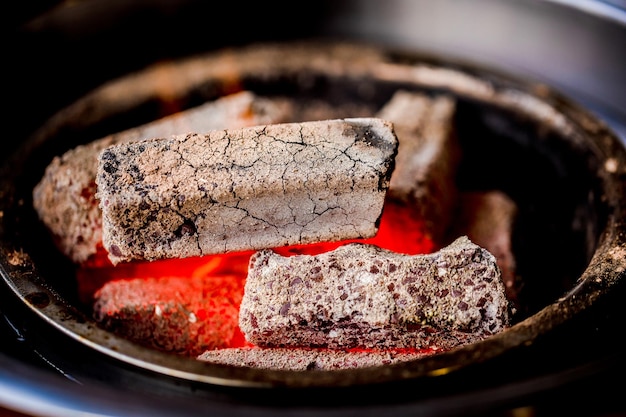 Trozo carbonizado con cenizas en la estufa, cubos de carbón para cocinar.