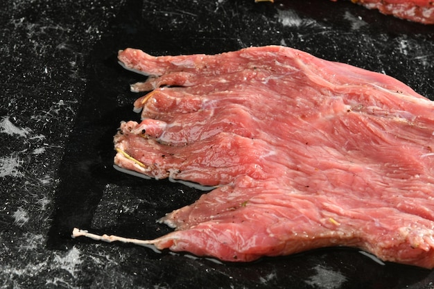 Un trozo de carne está sobre una superficie negra con un palo de ajo.