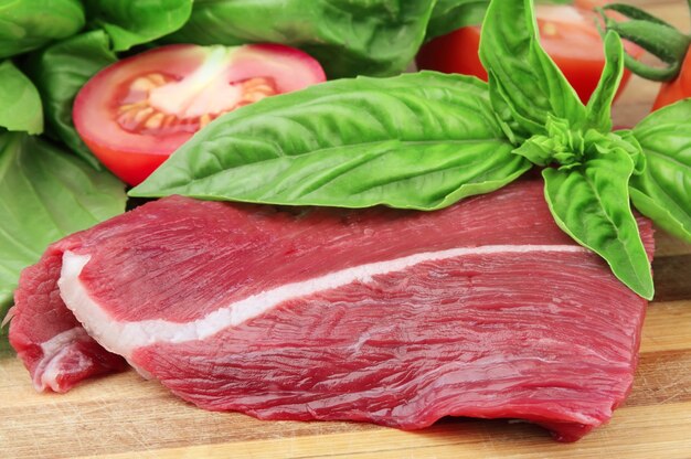 Foto trozo de carne fresca de basílicas y un tomate en una pizarra de madera