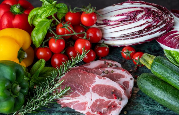 Trozo de carne fresca, especias y verduras variadas en tablero de mármol verde oscuro