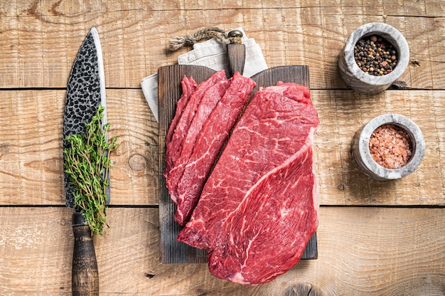 Trozo de carne de vacuno cruda de mármol en rodajas sobre tabla de cortar de madera. fondo de madera. Vista superior.