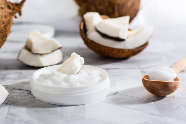 Un trozo de coco en aceite de coco en un frasco y una cuchara de madera con aceite y coco sobre la mesa