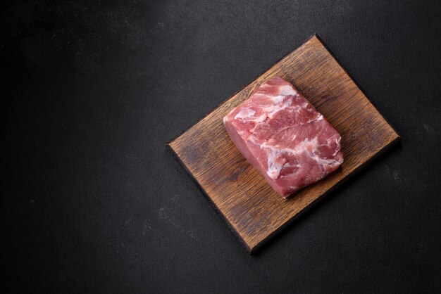 Trozo fresco de carne de cerdo cruda con especias, sal y hierbas en una tabla de cortar de madera