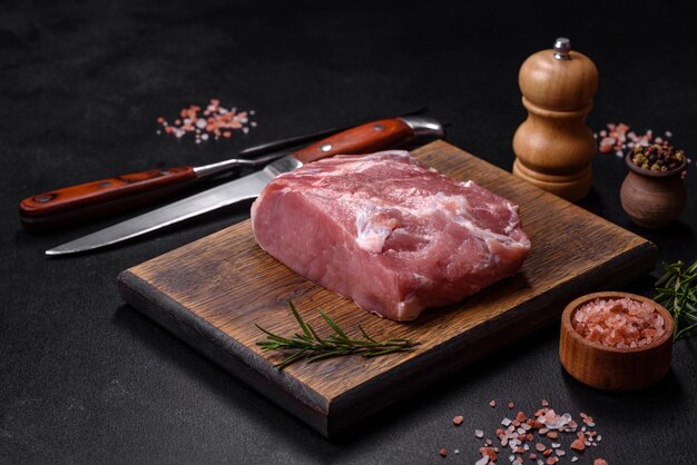 Trozo fresco de carne de cerdo cruda con especias, sal y hierbas en una tabla de cortar de madera