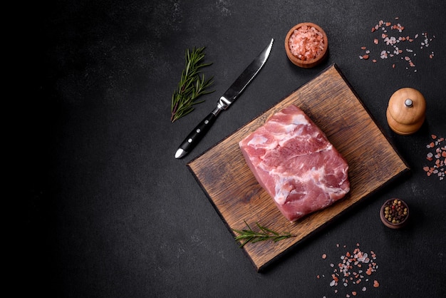 Trozo fresco de carne de cerdo cruda con especias, sal y hierbas en una tabla de cortar de madera