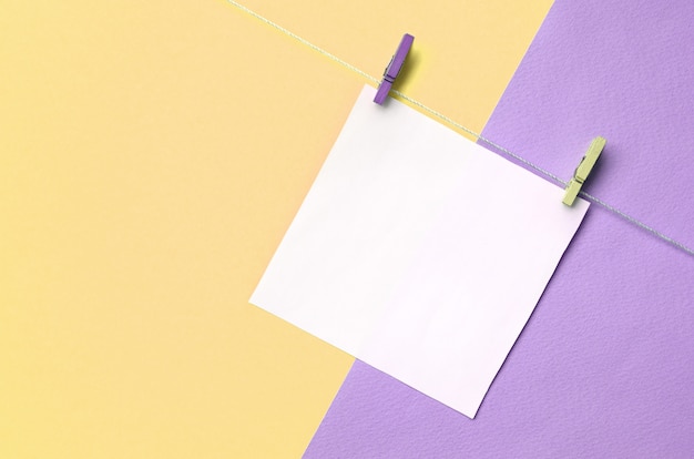 Un trozo de papel cuelga de una cuerda con clavijas en la textura de los colores amarillo y violeta pastel.