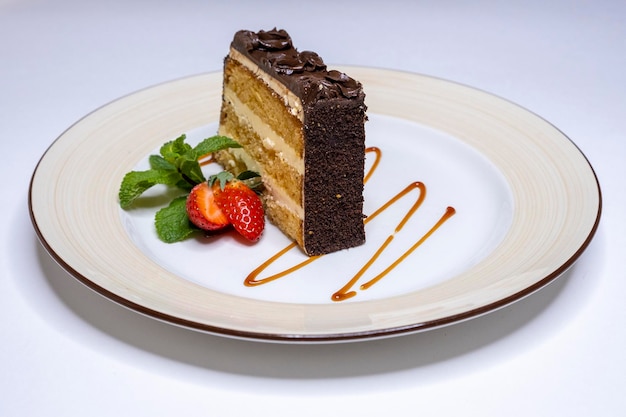 Un trozo de pastel de chocolate con crema de mantequilla en un plato blanco Postre de galleta dulce con bayas Menú de cafetería Comida nociva Pedazo de pastel cortado con fresas