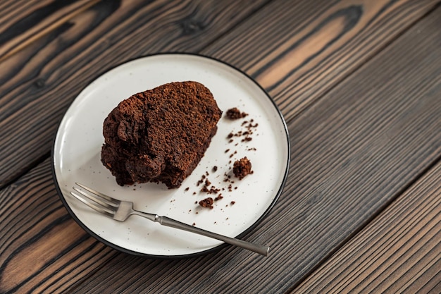 Un trozo de pastel de chocolate y un tenedor de postre en un plato blanco en el espacio de copia de la mesa de madera
