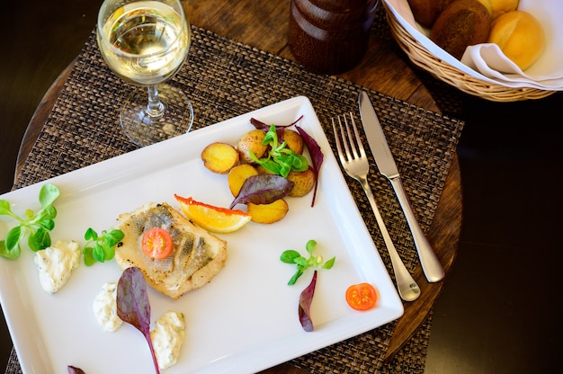 Un trozo de pescado con verduras y papas fritas en un plato