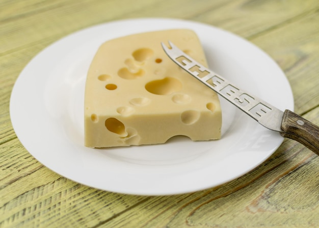 Un trozo de queso con agujeros y un cuchillo para cortar en un plato blanco.