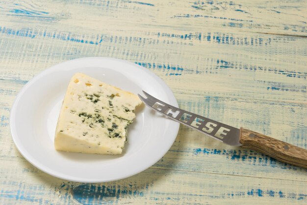 Un trozo de queso azul en un plato con un cuchillo de queso sobre un fondo de madera