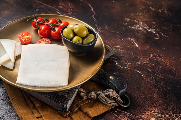 Trozo de queso de cabra duro en un plato con aceitunas y tomate Fondo oscuro Vista superior Espacio de copia