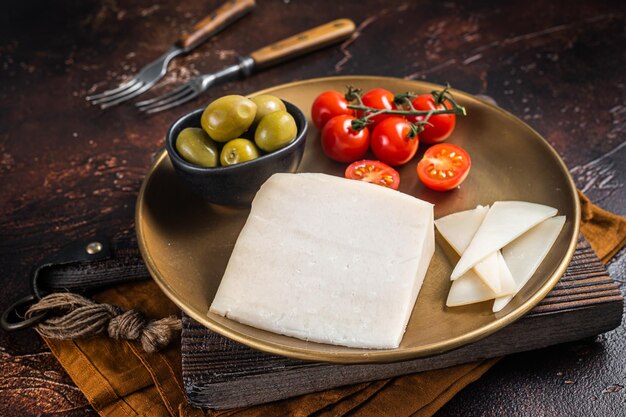 Trozo de queso de cabra duro en un plato con aceitunas y tomate Fondo oscuro Vista superior