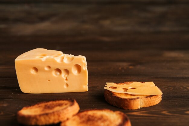 Trozo de queso con grandes agujeros y pan frito en una mesa de madera. Sandwich con queso.